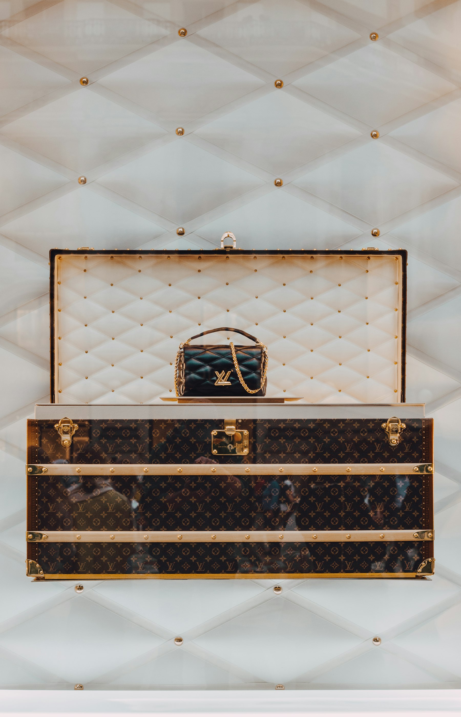 An opened monogrammed courier trunk displaying a quilted leather handbag.
