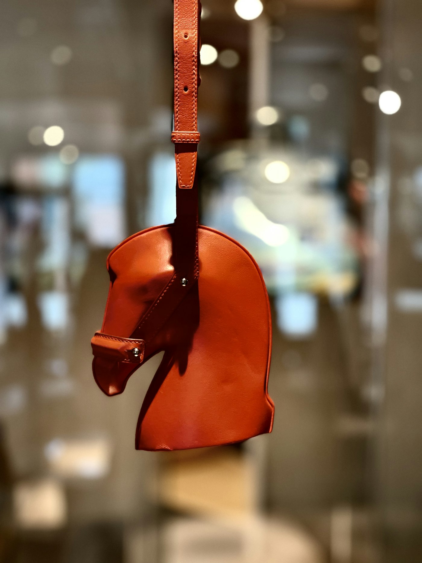 A sculptural leather bag in the shape of a horse's head, hanging by its strap.